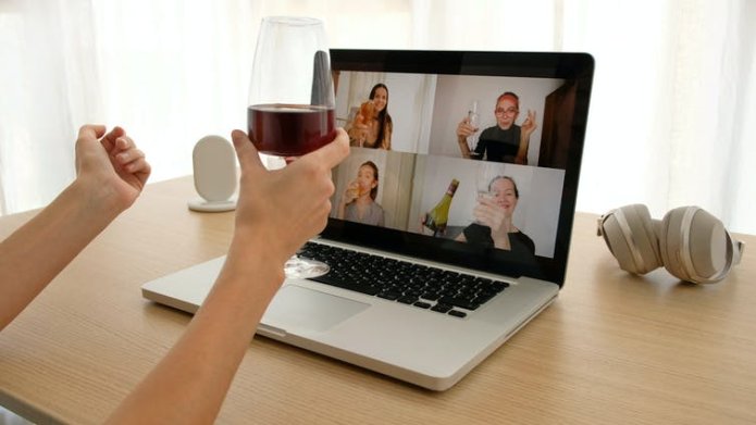 Woman drinks wine in front of laptop showing video call.