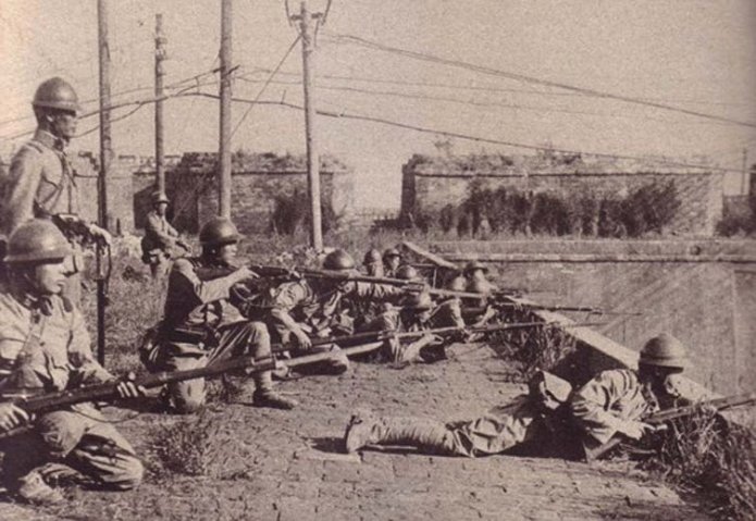 Japanese soldiers standing and lying pointing guns.