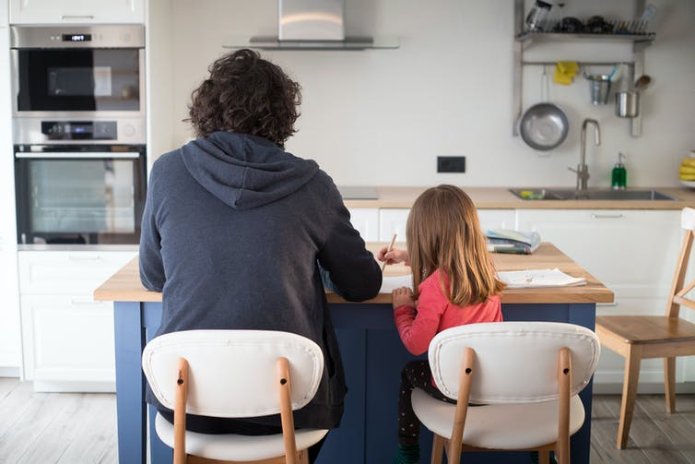 A man helps his daughter with schoolwork at the kitchen table.