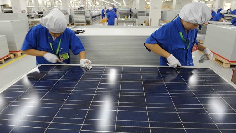 Two workers with white gloves work on a solar panel.