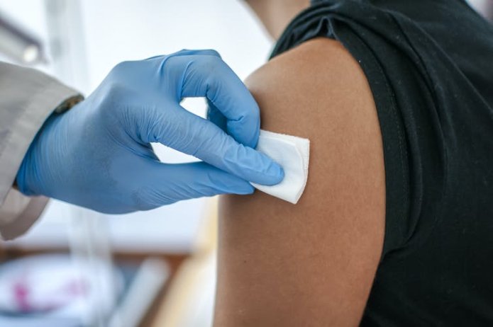 A medical professional wearing gloves disinfects a patient's arm ahead of vaccination.