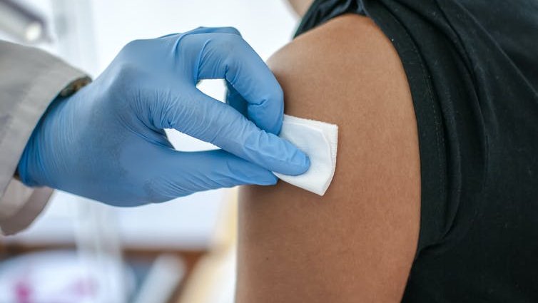 A medical professional wearing gloves disinfects a patient's arm ahead of vaccination.