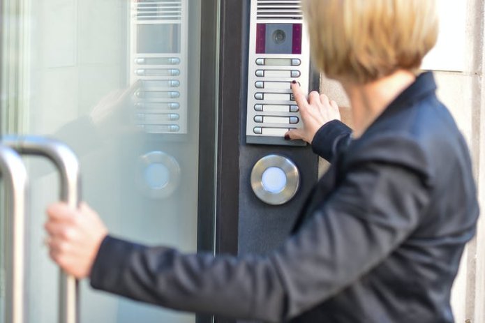 A woman using an intercom and pulling open a door