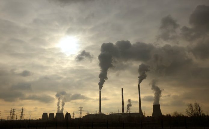 Smoke coming out of chimnies with sun emerging from the clouds above.