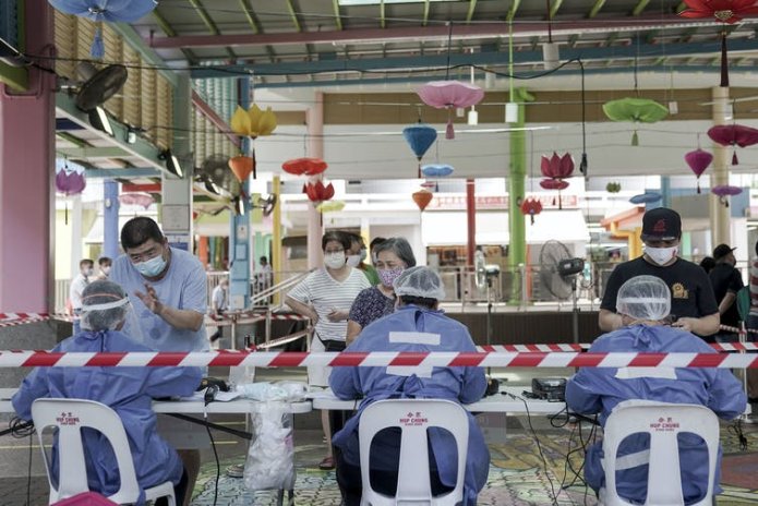 Workers in PPE register people at a table with colourful lights hanging behind.