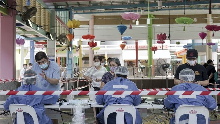 Workers in PPE register people at a table with colourful lights hanging behind.