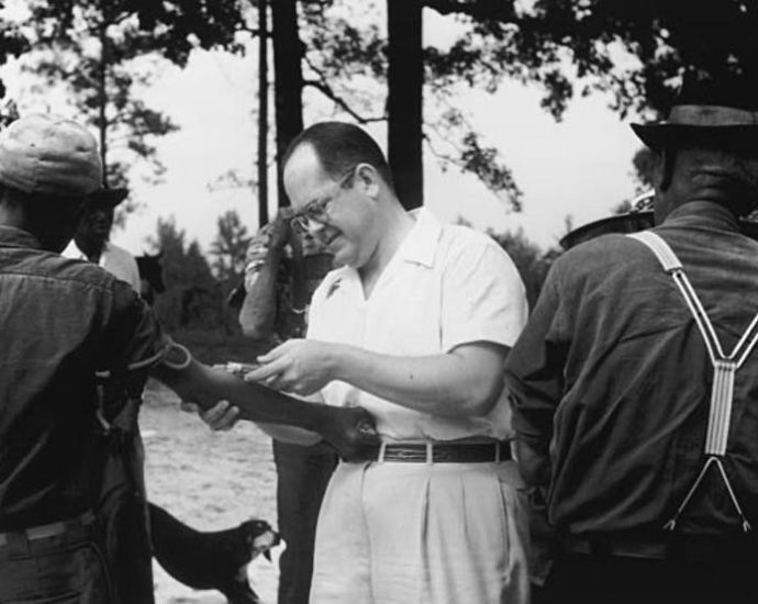 A Black participant in the Tuskegee Syphilis Study has blood drawn by a white man.