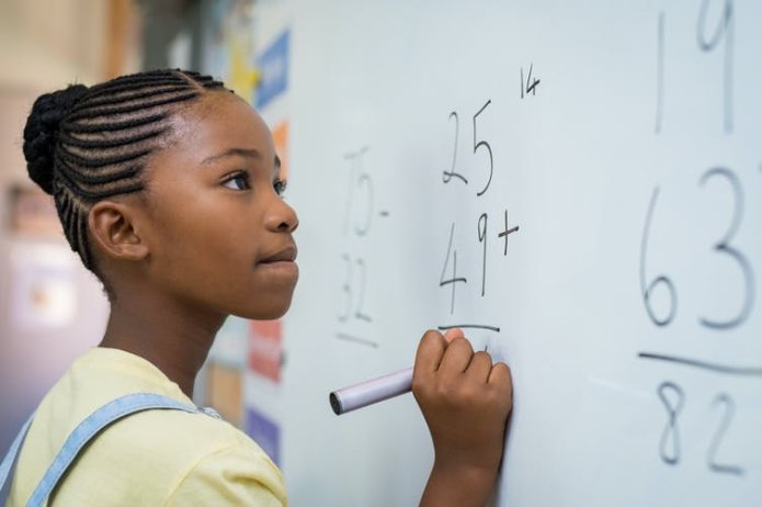 Young girl solving maths problem on whiteboard