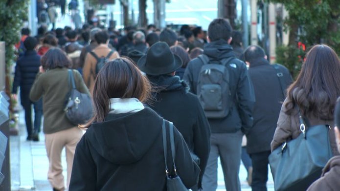 Japanese commuters photographed from behind, including several women.