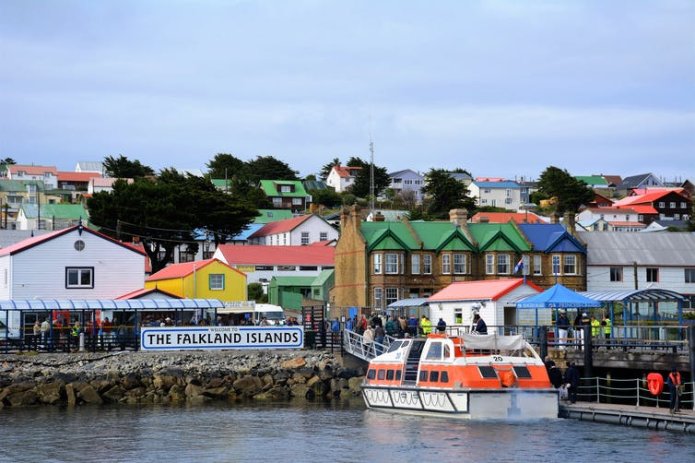 An orange tender boat brings visitors ashore from a cruise boat.