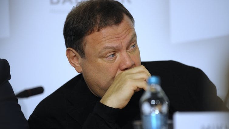 Russian businessman Mikhail Fridman sits with his hand over his mouth and a bottle of water in front of him.