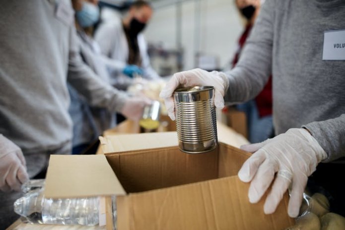 Close up of volunteers' hands placing canned donations in cardboard boxes.