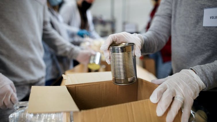Close up of volunteers' hands placing canned donations in cardboard boxes.