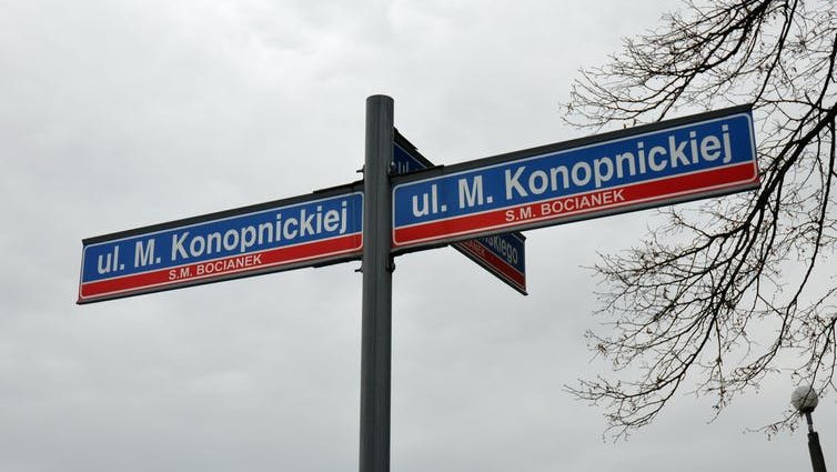 A set of red and blue street name signs seen against a cloudy sky.