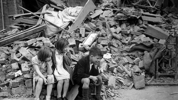 Children sit among the rubble of houses destroyed in the Blitz, London 1941.