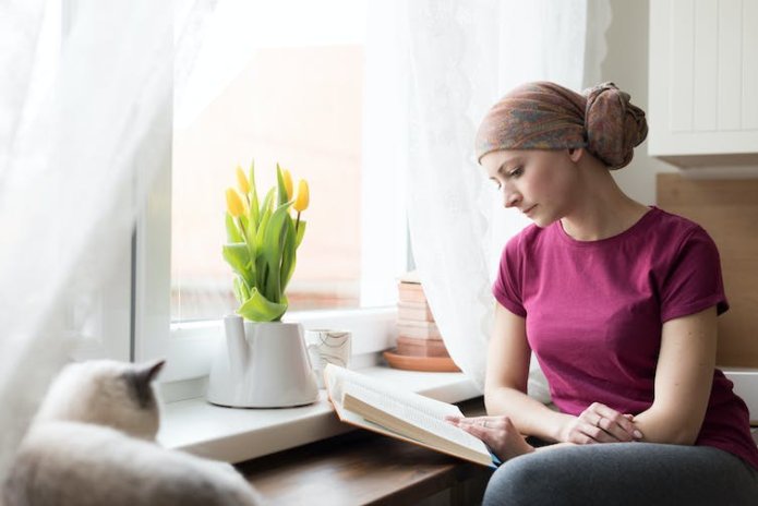 A woman wearing a head scarf is reading a book at home.