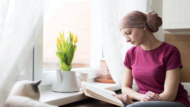 A woman wearing a head scarf is reading a book at home.