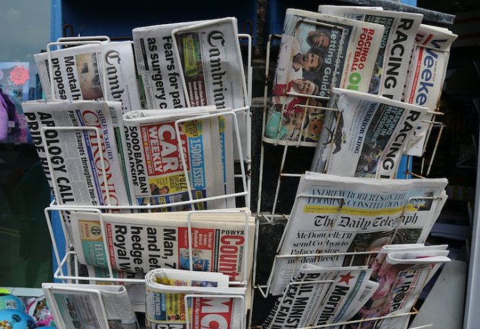 A selection of different newspaper brands are stacked in a display.